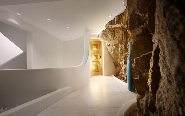 Pasillo de diseño moderno con pared de roca natural y puerta dorada en Cavo Tagoo Mykonos