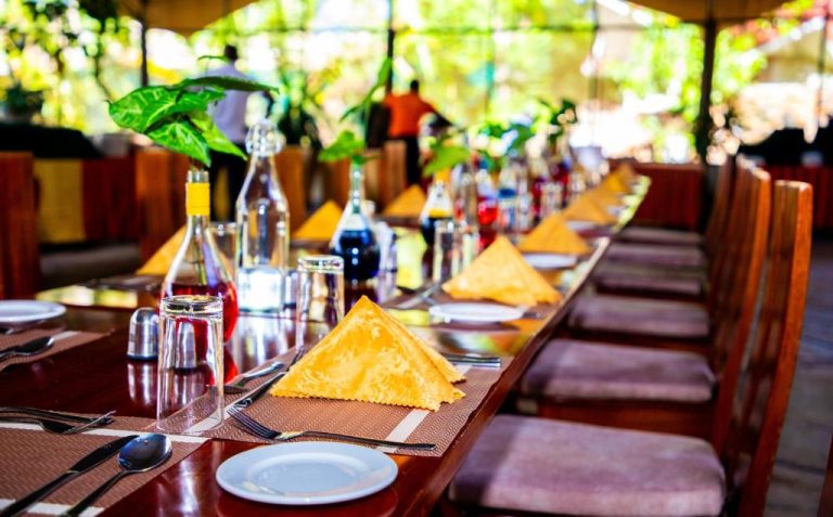 Mesa elegante con servilletas doradas en el restaurante de terraza exterior del Kisimani Eco Resort & Spa