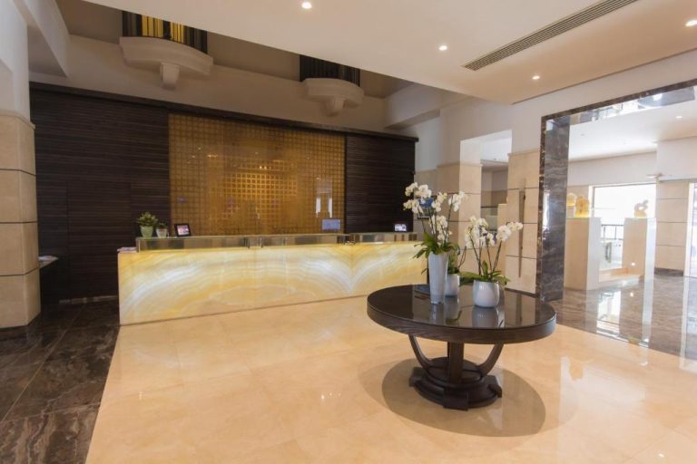Recepción principal con mostrador iluminado y flores blancas en el lobby del Maritim Antonine Hotel & Spa