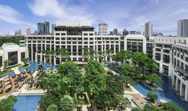 Vista aérea de las piscinas y jardines tropicales del Siam Kempinski Hotel Bangkok con skyline al fondo