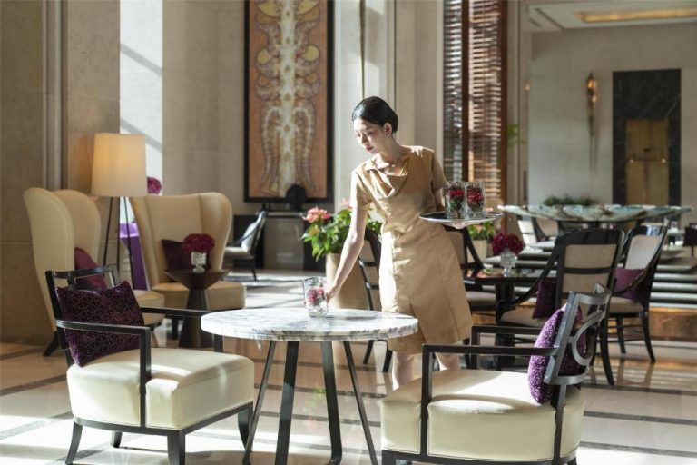 Camarera sirviendo té en el elegante lobby del Siam Kempinski Hotel Bangkok con decoración de lujo