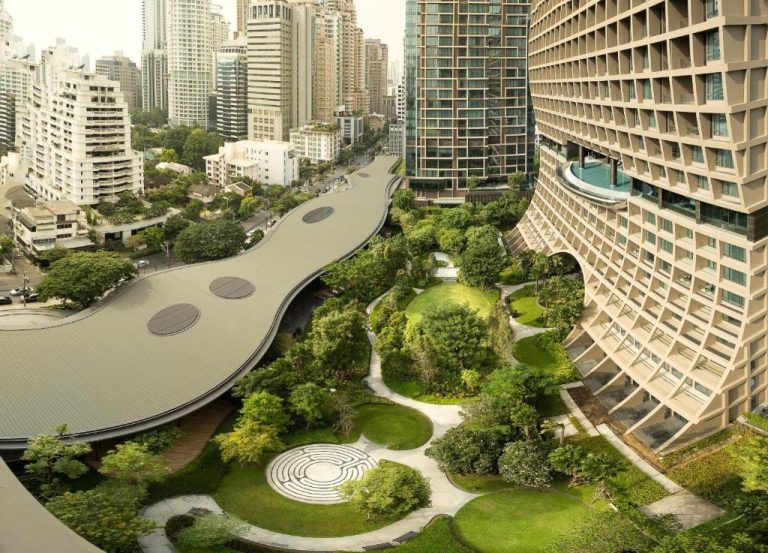Jardín tropical con senderos y zona verde del Sindhorn Kempinski Hotel Bangkok entre rascacielos