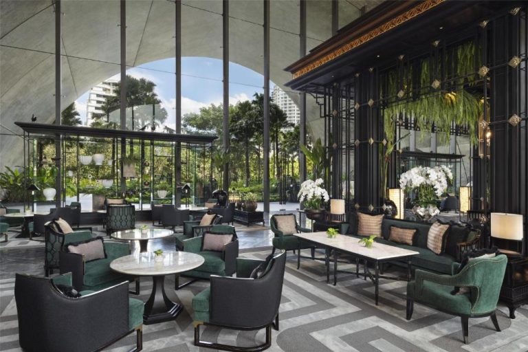 Elegante lobby lounge con sillones verdes y vistas al jardín tropical del Sindhorn Kempinski Hotel Bangkok