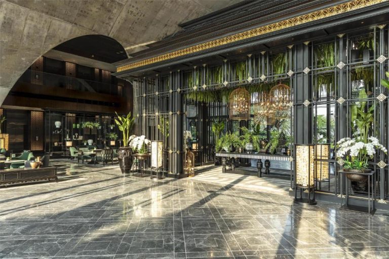 Lujoso lobby del Sindhorn Kempinski Hotel Bangkok con plantas tropicales, suelo de mármol y decoración dorada