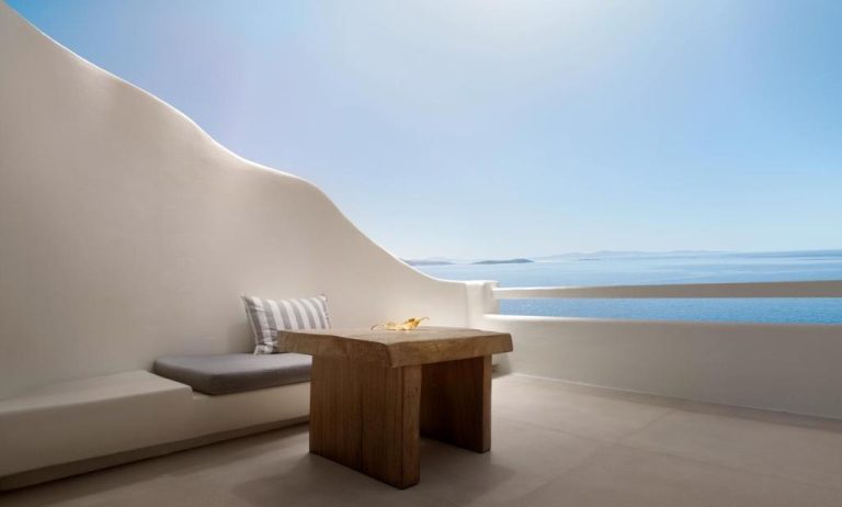 Terraza con banco empotrado y mesa de madera con vistas al mar Egeo en Cavo Tagoo Mykonos