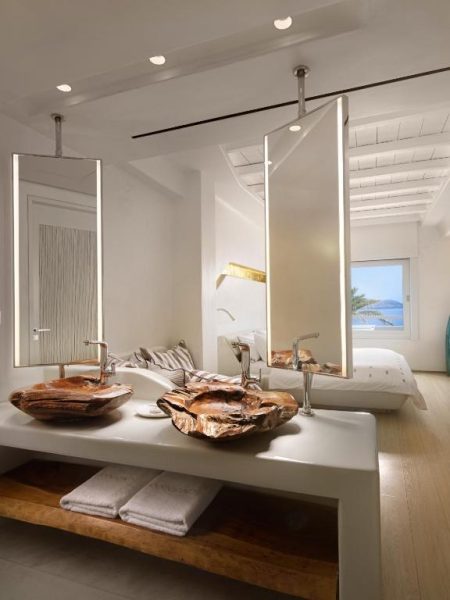 Baño de lujo con lavabos de madera petrificada y espejos iluminados en Cavo Tagoo Mykonos