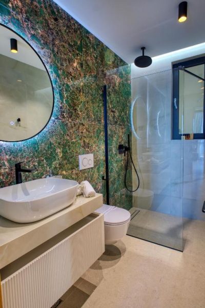Baño de lujo con mármol verde, ducha encastrada y lavabo sobre encimera en La Dolce Villa