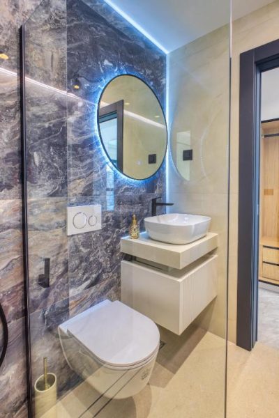 Baño de lujo con paredes de mármol, lavabo sobre encimera y espejo redondo con luz LED en La Dolce Villa