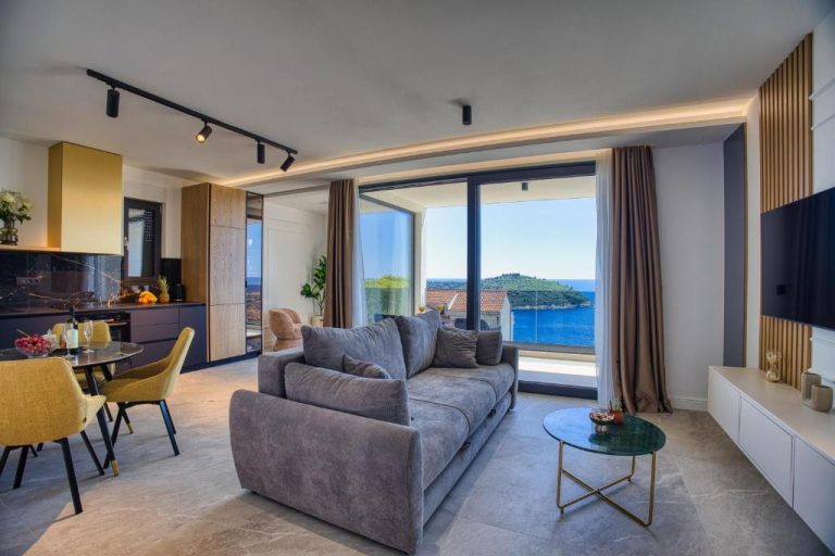 Salón moderno con sofá gris y vistas al mar en La Dolce Villa, con cocina abierta y terraza