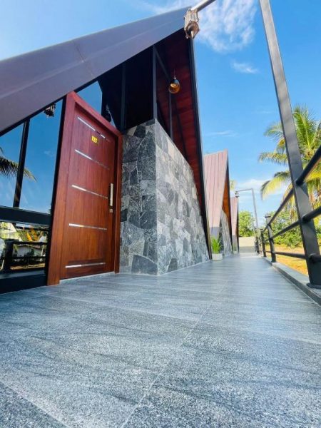 Entrada principal del Hotel Avinka Grand con puerta de madera, revestimiento de piedra y suelo de granito