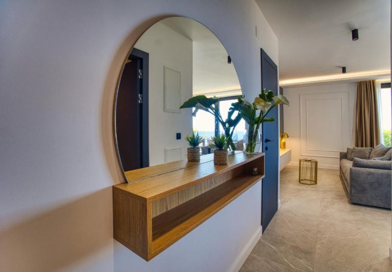 Entrada con espejo circular y consola de madera en La Dolce Villa 1, con salón moderno al fondo