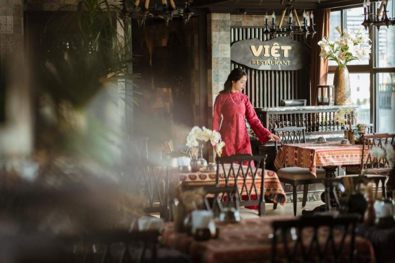 Restaurante Việt del GM Premium Hotel con decoración tradicional vietnamita y camarera con vestido rojo