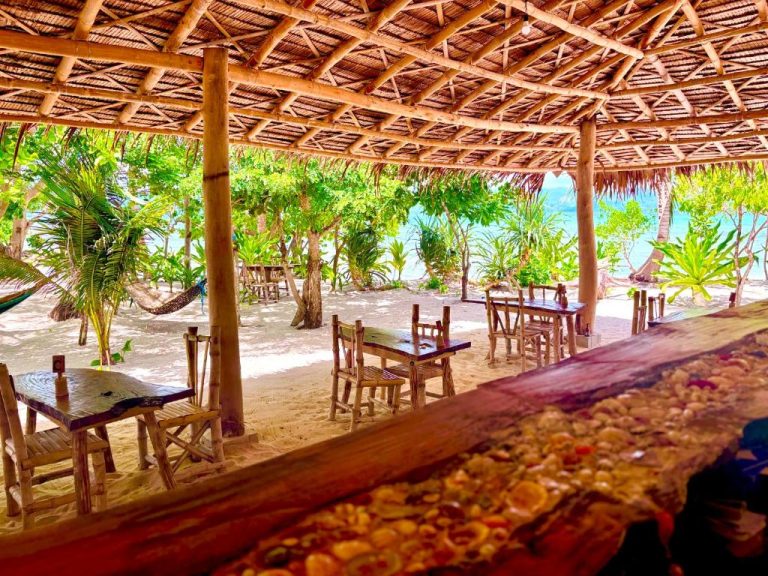 Restaurante al aire libre con techo de palma y mesas de madera frente a la playa en Dos Playa EcoCamp Daracoton Island