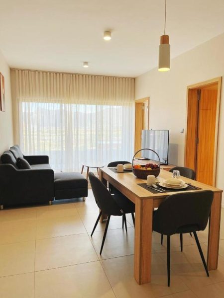 Salón comedor moderno con mesa de madera y sofá en Minissy Suites, amplia ventana con luz natural