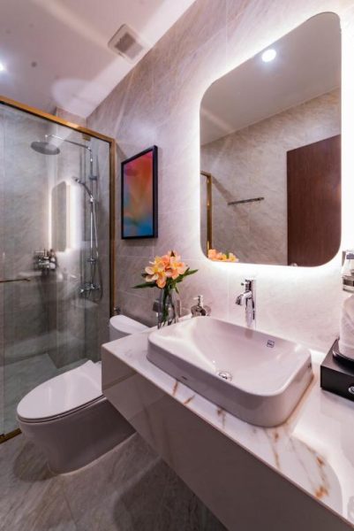 Baño de lujo con ducha de cristal, lavabo sobre encimera de mármol y espejo con luz en Anise Luxe Home