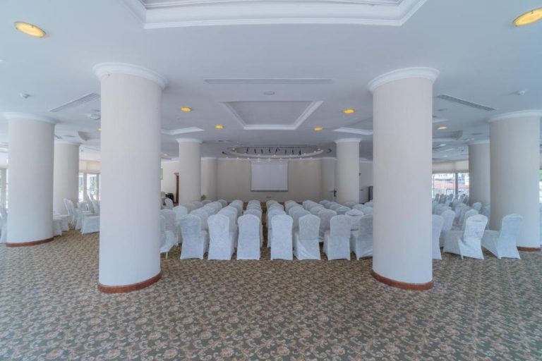 Salón de conferencias con sillas blancas y pantalla de proyección en Pineta Park Deluxe Hotel All Inclusive