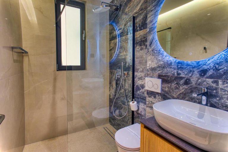 Baño de lujo con ducha, lavabo sobre encimera y pared de mármol azul en La Dolce Villa 1