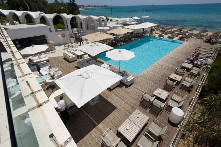 Piscina exterior con terraza de madera y tumbonas frente al mar en The Sindbad Hotel