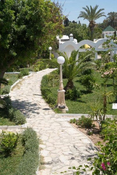 Jardín con camino de piedra, farolas blancas y palmeras del hotel The Sindbad en Túnez