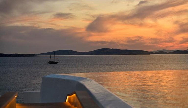 Piscina infinita con vistas al mar y velero al atardecer en Anax Resort and Spa Mykonos