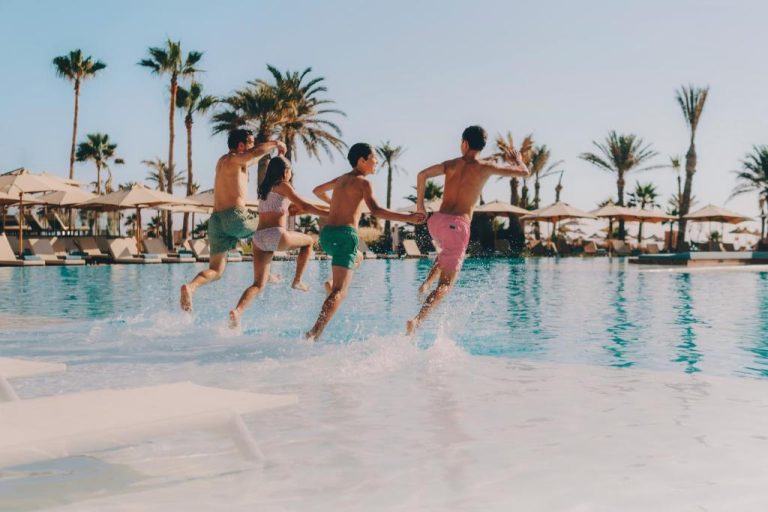 Grupo de amigos saltando a la piscina exterior del Iberostar Selection Eolia Djerba entre palmeras