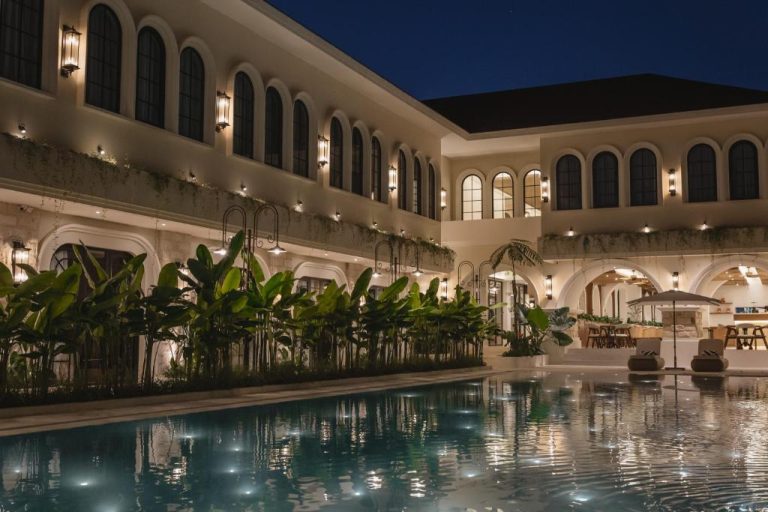 Piscina exterior iluminada de noche en Hygge Hotel and Villas Seminyak con jardín tropical y fachada colonial