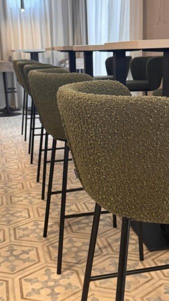 Taburetes altos tapizados en verde del bar del Hotel Aquarius Dubrovnik con mesas altas de madera