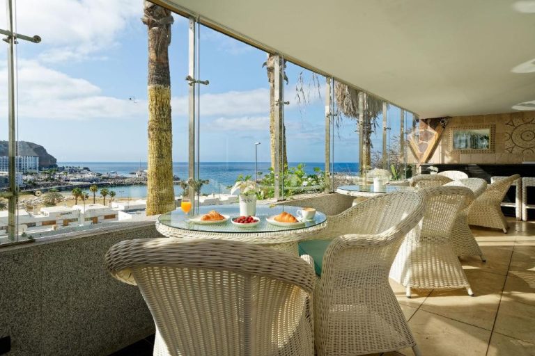 Terraza con desayuno y vistas al mar del Aparthotel Maracaibo con sillas de mimbre blancas