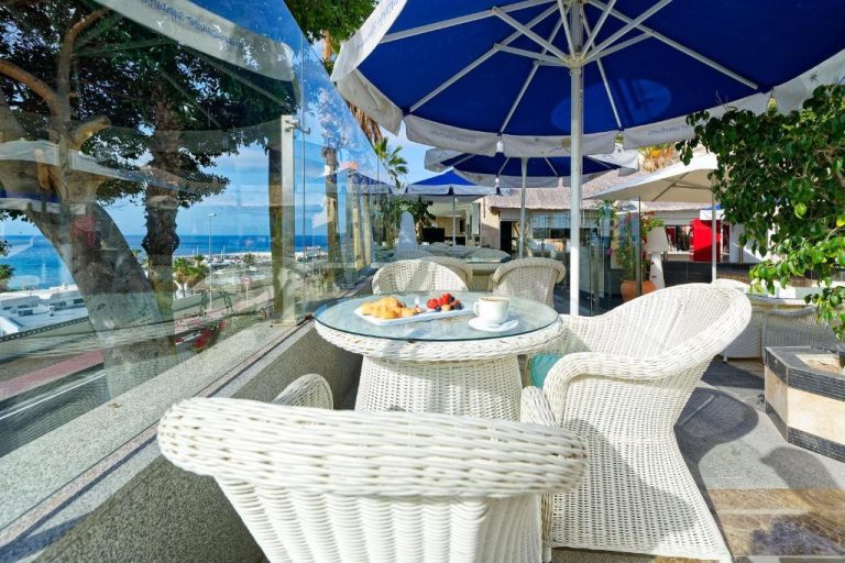 Terraza exterior con sillas de ratán blanco y desayuno servido en Aparthotel Maracaibo con vistas al mar