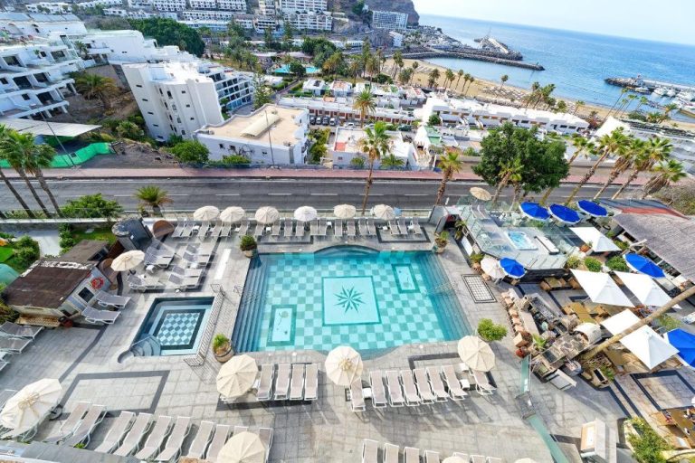 Piscina exterior con tumbonas y sombrillas del Aparthotel Maracaibo con vistas al puerto y playa