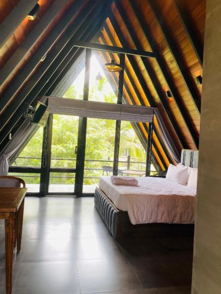 Habitación tipo cabaña con techo triangular de madera y gran ventanal con vista al jardín en Avinka Grand