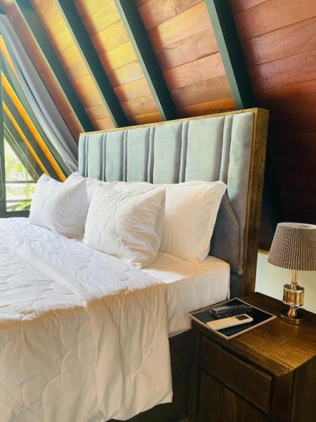 Habitación con cama doble y cabecero tapizado en cabaña de madera del hotel Avinka Grand