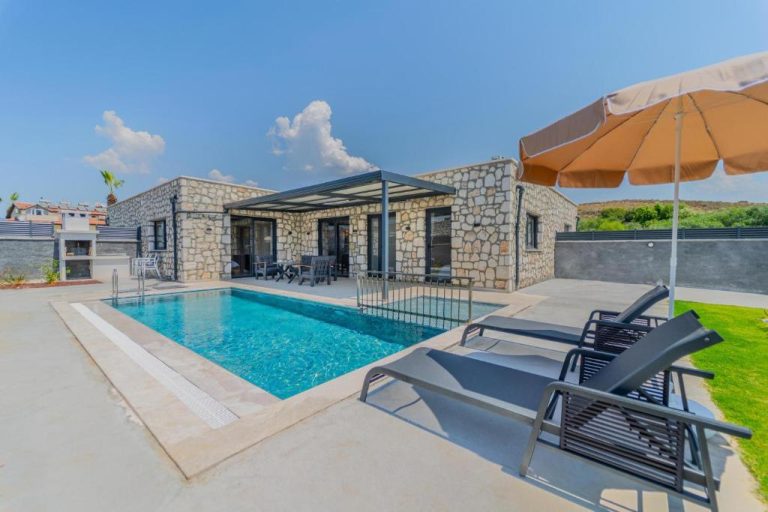 Piscina privada con tumbonas y sombrilla en Zora Beyaz Taş Villaları con fachada de piedra