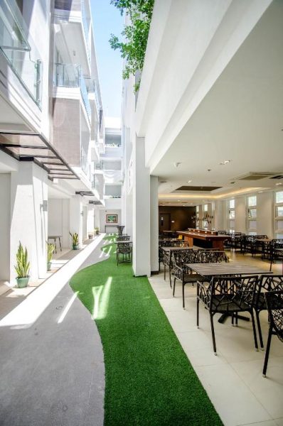Terraza con jardín verde y restaurante interior del Boracay Haven Suites con mesas y sillas decorativas