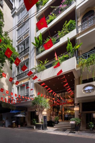 Fachada exterior del Le Premier Hotel & Rooftop Bar decorada con banderas rojas vietnamitas y balcones con plantas