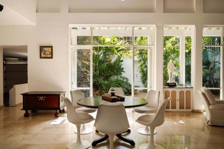 Comedor con sillas blancas y vistas al jardín tropical en Jetwing Ratnam Residence