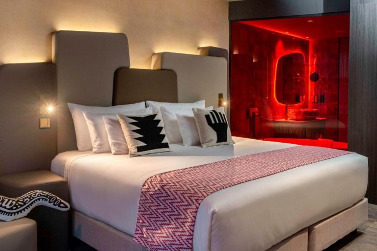 Habitación de lujo con cama doble y baño acristalado de iluminación roja en el hotel Nhow Lima