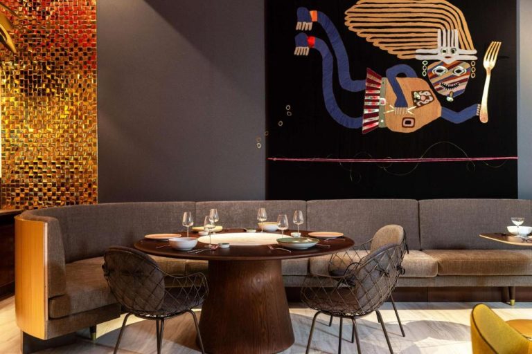 Restaurante del Nhow Lima con mesa redonda, sofá y mural artístico de estilo precolombino en la pared