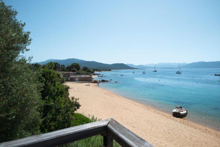 Playa de arena dorada con aguas turquesas y veleros en la bahía del Hotel L'Escale en Córcega