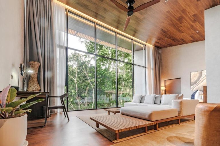 Sala de estar con sofá blanco, techo de madera y ventanales panorámicos con vistas al bosque en Piece Lio from Japan