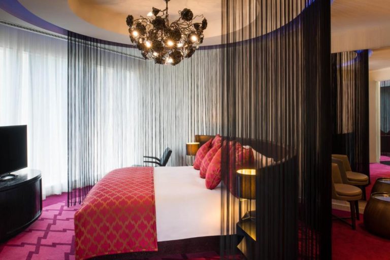 Suite de lujo del W Doha con cortinas negras, cama king y lámpara araña artística