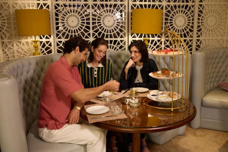 Tres personas disfrutando del afternoon tea en el elegante salón del W Doha con torre de postres