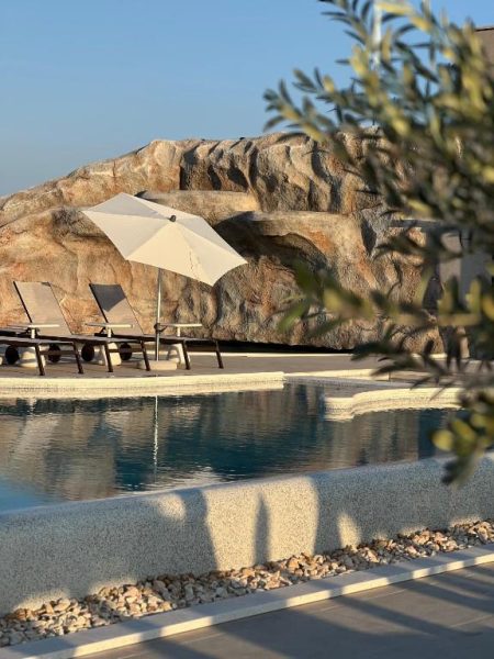Piscina exterior con tumbonas y sombrilla blanca junto a rocas naturales en Hotel Sumratin