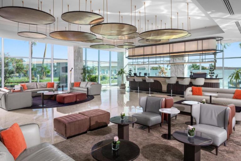 Elegante lobby bar con sofás grises y cojines naranja en Pickalbatros Golf Luxury Suites All Inclusive