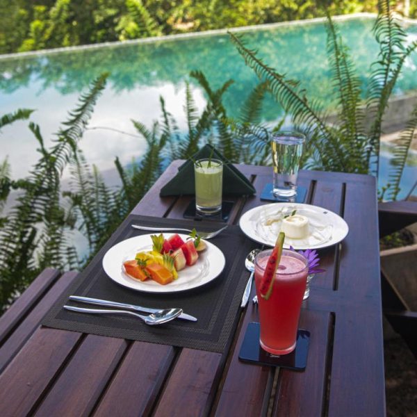 Desayuno tropical con zumos frescos y frutas junto a la piscina infinita del AHAS GAWWA Eco Lodge