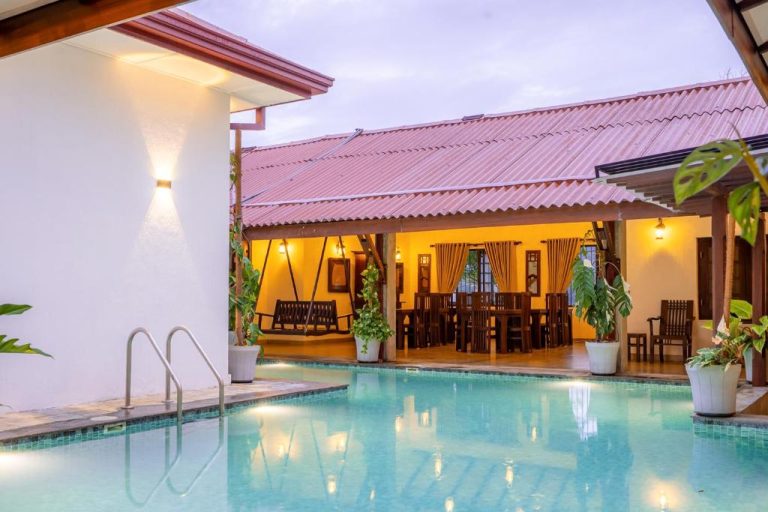 Piscina exterior con terraza cubierta e iluminada del hotel The Tusker's Hideout rodeada de plantas tropicales