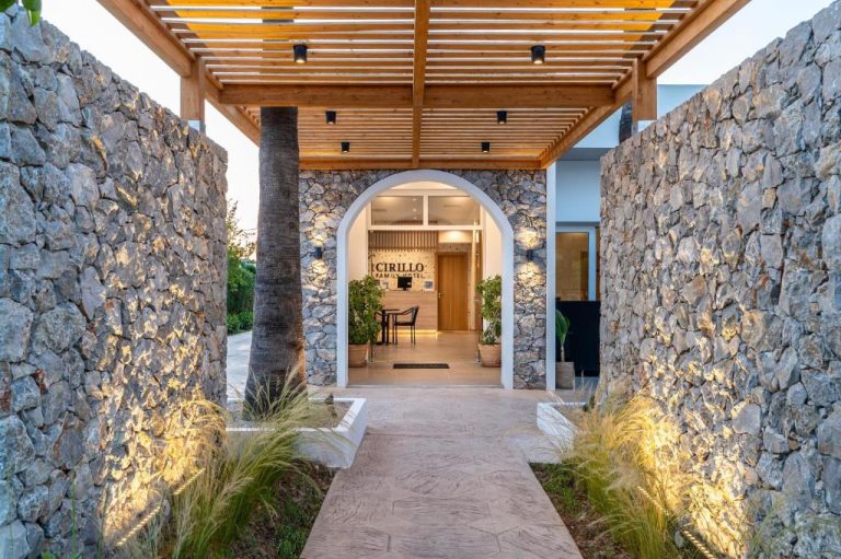 Entrada principal del Cirillo Family Hotel con arco blanco, paredes de piedra y pérgola de madera iluminada