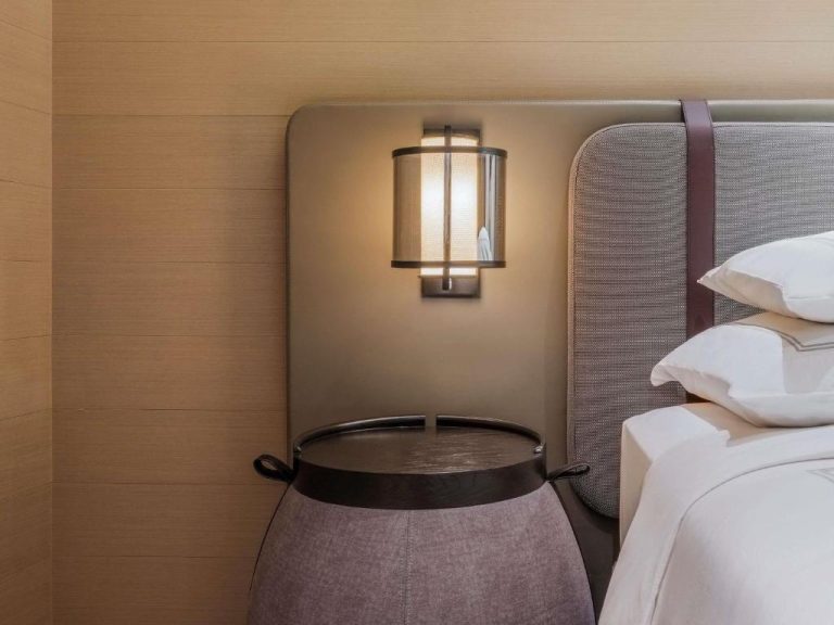 Mesita de noche de diseño con lámpara de pared y cabecero tapizado en Swissotel The Stamford Singapore