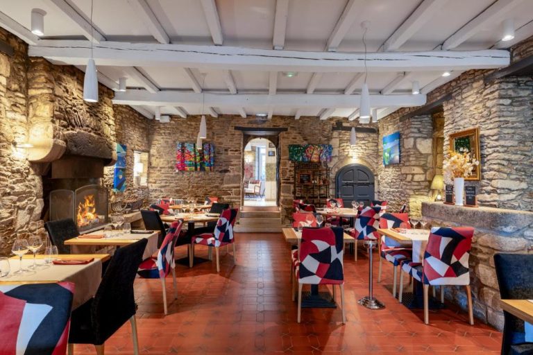 Salón comedor rústico con chimenea encendida y paredes de piedra en Hotel Restaurant Lesage