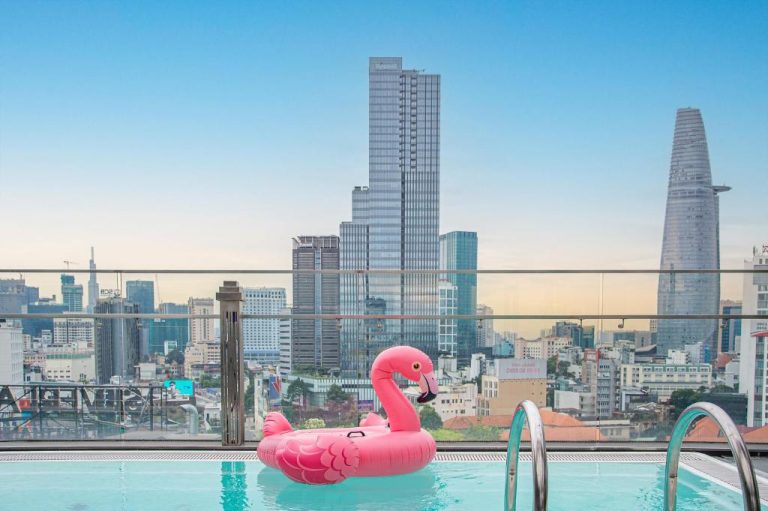 Piscina rooftop con flamenco hinchable rosa y vistas al skyline de Ho Chi Minh en Winsuites Saigon Hotel